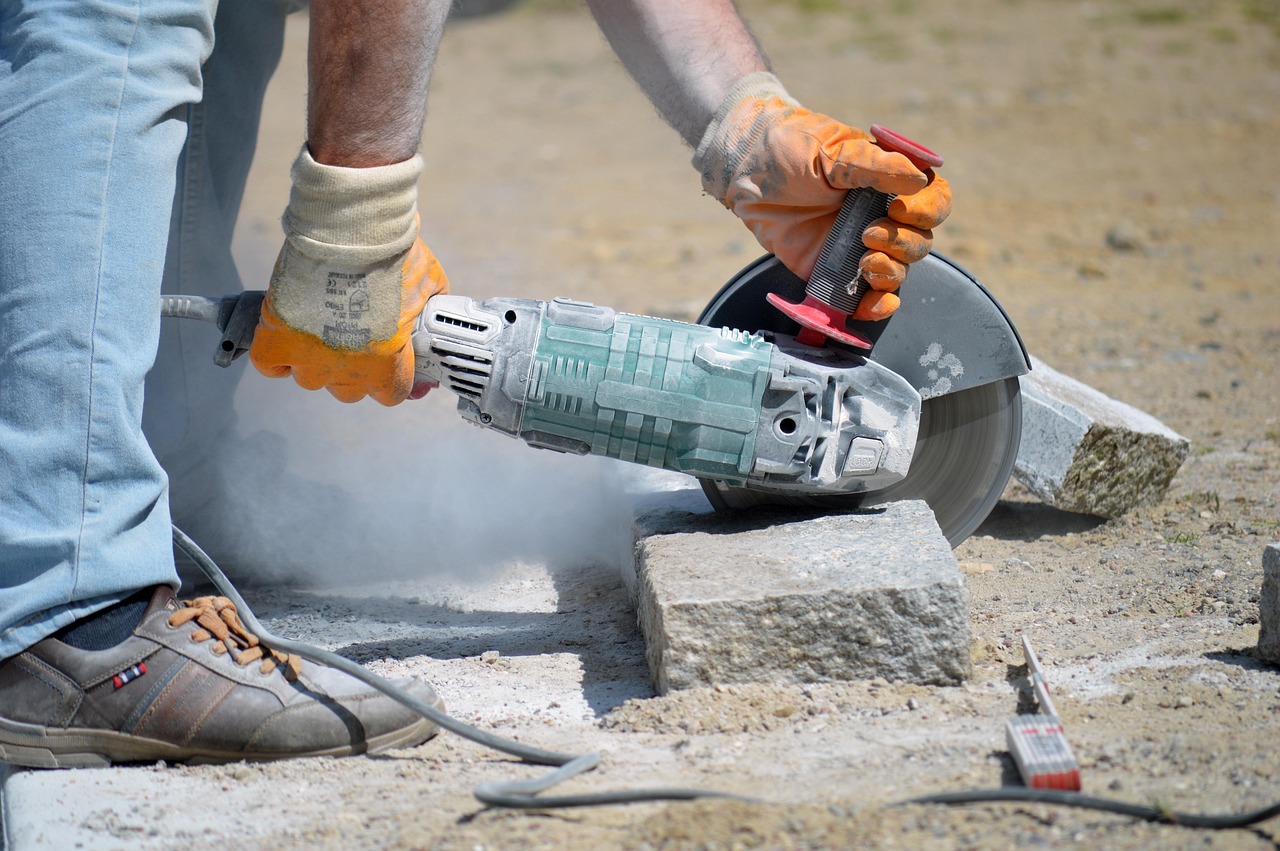 A close-up photo of a man cutting a concrete block with dust.